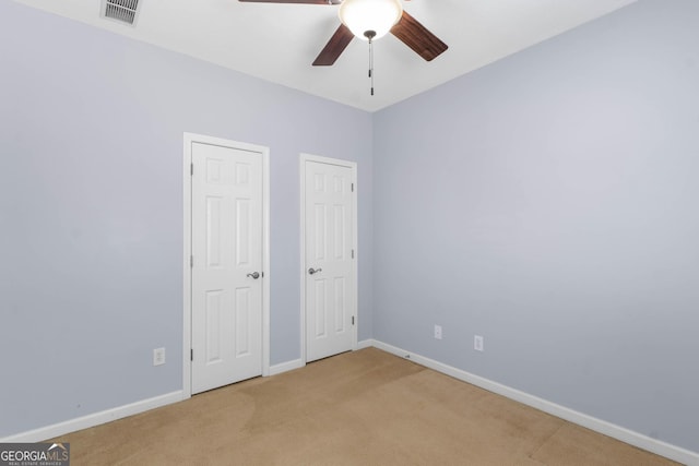 unfurnished bedroom featuring two closets, a ceiling fan, visible vents, light carpet, and baseboards