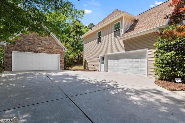view of property exterior featuring concrete driveway, roof with shingles, stone siding, and a garage