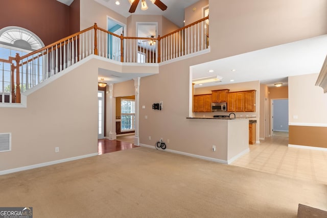 unfurnished living room with a towering ceiling, baseboards, light colored carpet, and ceiling fan