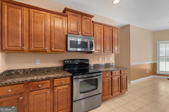 kitchen with baseboards, stainless steel appliances, dark stone countertops, and brown cabinets
