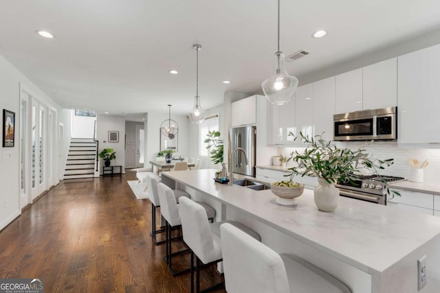 kitchen with white cabinets, stainless steel appliances, a center island with sink, visible vents, and light countertops