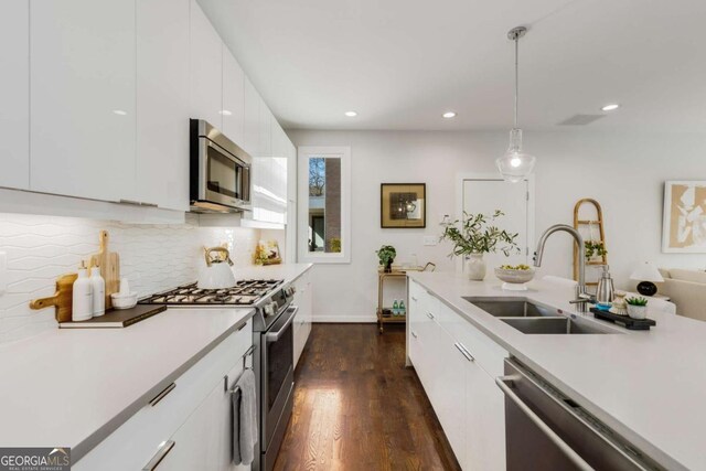 kitchen with stainless steel appliances, a sink, tasteful backsplash, white cabinetry, and light countertops