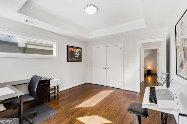 office space featuring a tray ceiling, wood finished floors, visible vents, and baseboards
