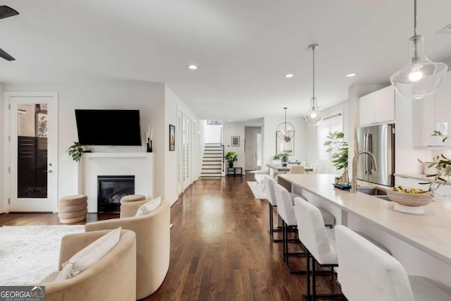 living area with stairway, a glass covered fireplace, dark wood-style flooring, visible vents, and recessed lighting