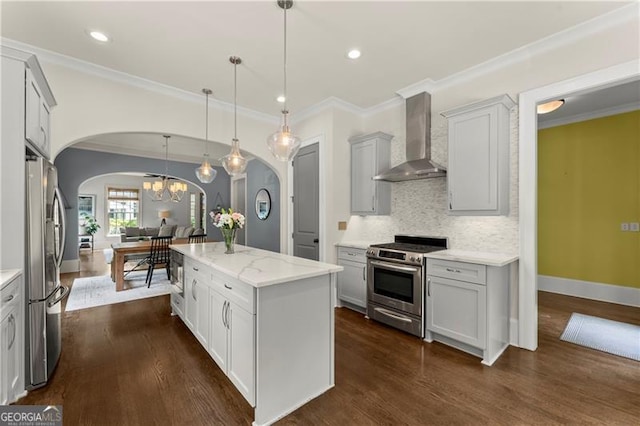 kitchen with wall chimney range hood, crown molding, appliances with stainless steel finishes, arched walkways, and dark wood finished floors