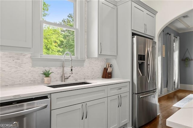 kitchen with arched walkways, appliances with stainless steel finishes, a sink, and tasteful backsplash
