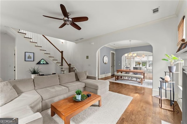 living room featuring visible vents, wood finished floors, stairway, arched walkways, and ceiling fan with notable chandelier