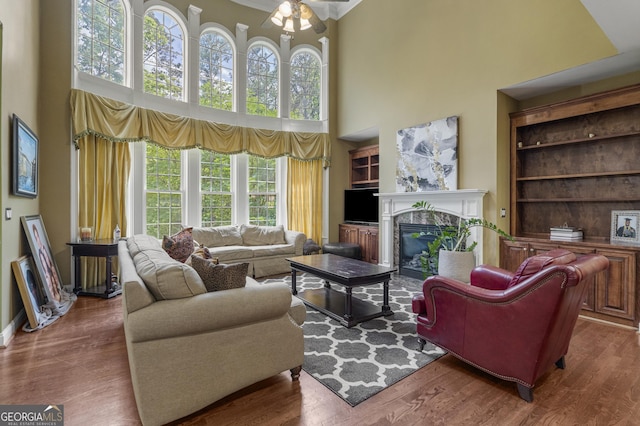 living area featuring ceiling fan, a fireplace, wood finished floors, and a towering ceiling