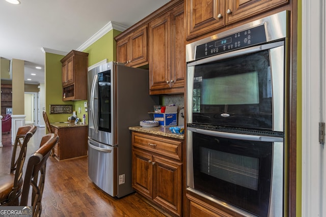 kitchen featuring appliances with stainless steel finishes, ornamental molding, dark wood finished floors, and light stone counters