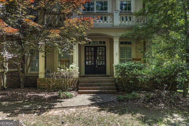 view of exterior entry with french doors, a balcony, and covered porch