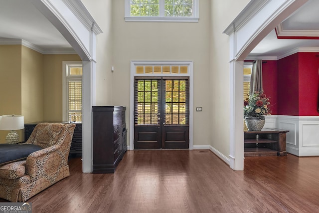 foyer entrance featuring arched walkways, a healthy amount of sunlight, wood finished floors, and a towering ceiling