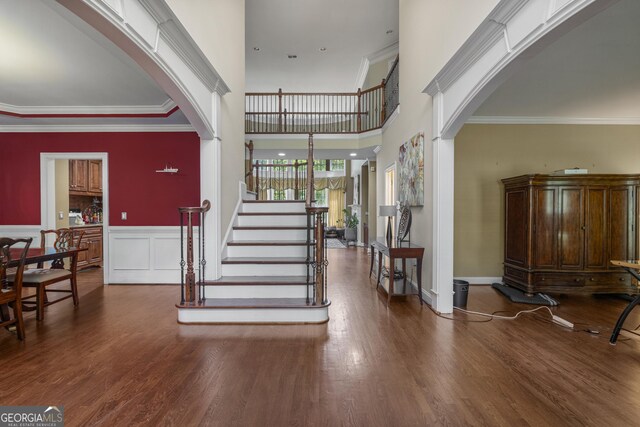 foyer entrance featuring ornamental molding, wood finished floors, stairway, a wainscoted wall, and arched walkways