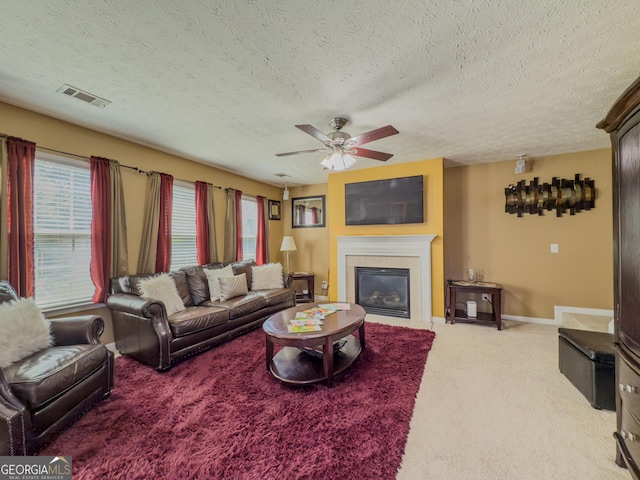 living room with carpet, visible vents, a glass covered fireplace, a textured ceiling, and ceiling fan