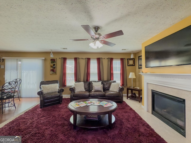 living area featuring a high end fireplace, a healthy amount of sunlight, a ceiling fan, and a textured ceiling