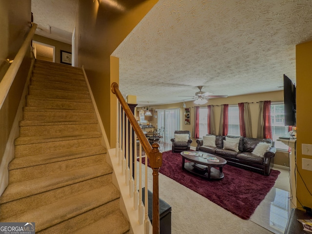 stairway with a ceiling fan, a textured ceiling, and carpet