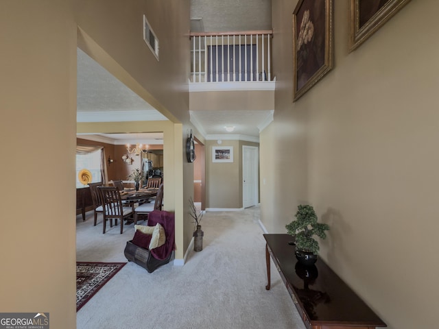carpeted entryway featuring baseboards, ornamental molding, a towering ceiling, and visible vents