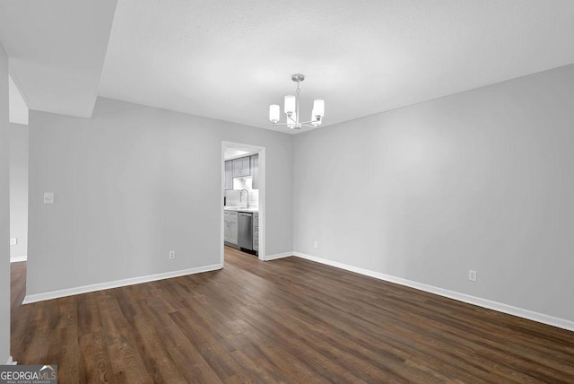 empty room featuring baseboards, a notable chandelier, a sink, and dark wood-type flooring