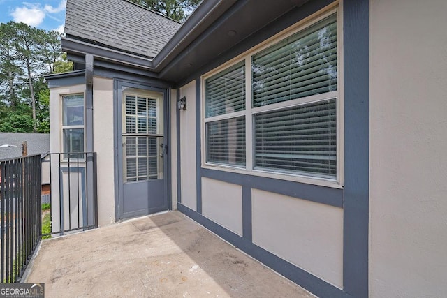view of exterior entry featuring roof with shingles and stucco siding