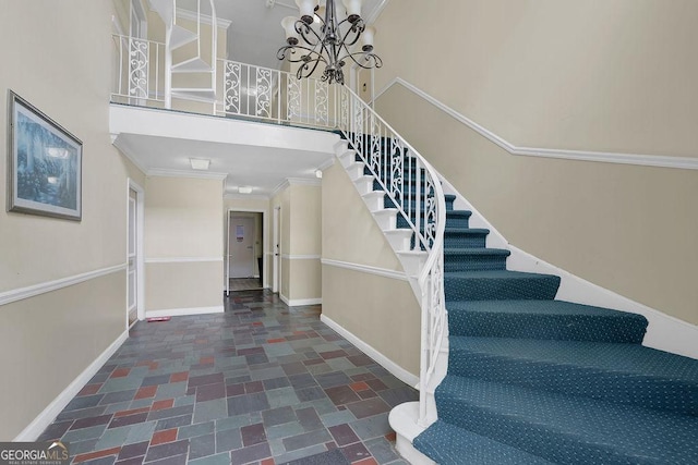 staircase with crown molding, a towering ceiling, baseboards, stone finish floor, and a chandelier