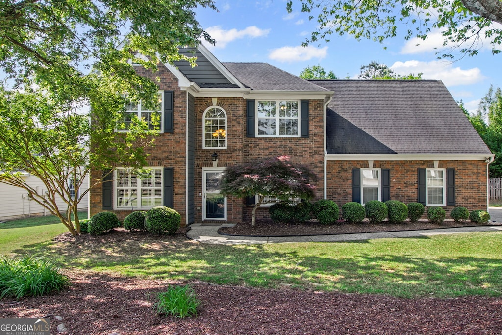 colonial-style house with brick siding, a front yard, and roof with shingles