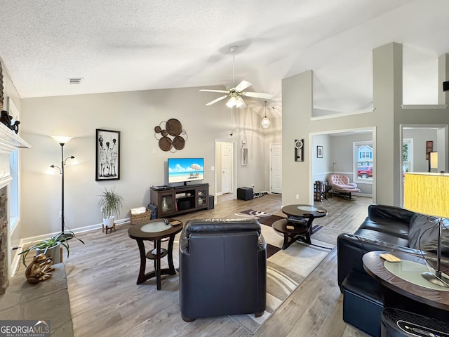 living area featuring visible vents, high vaulted ceiling, wood finished floors, ceiling fan, and a fireplace