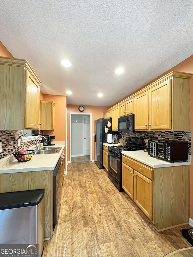 kitchen featuring backsplash, light countertops, a sink, light wood-style floors, and black appliances