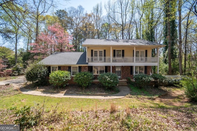 view of front facade featuring a front lawn, brick siding, a balcony, and covered porch