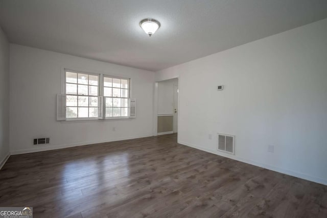 spare room with wood finished floors, visible vents, and baseboards
