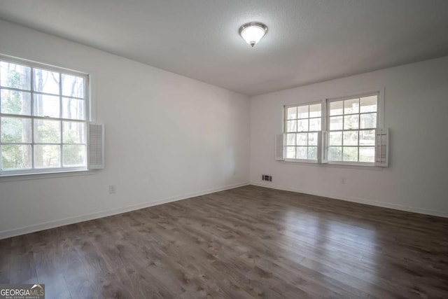 empty room featuring a healthy amount of sunlight, baseboards, dark wood-style flooring, and visible vents