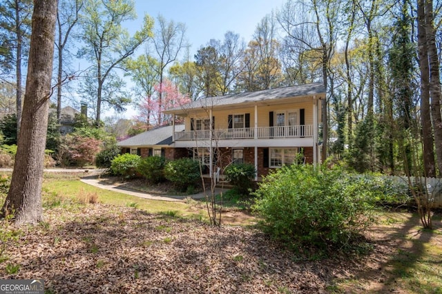 rear view of property featuring covered porch, a balcony, and brick siding