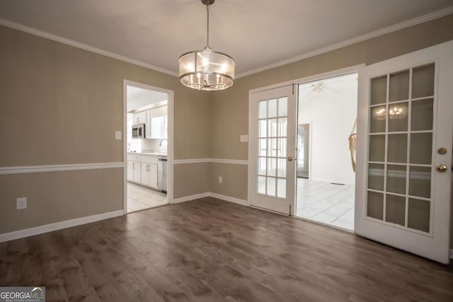 unfurnished dining area featuring baseboards, crown molding, wood finished floors, and a chandelier