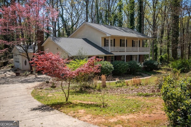 view of side of property with a chimney, a balcony, roof with shingles, and concrete driveway