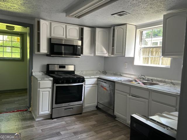 2016 Conrad Ave SE, Atlanta, GA 30315 - kitchen featuring wood finished floors, a sink, stainless steel appliances, white cabinets, and visible vents