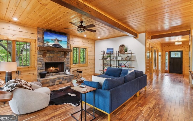 living room with wood walls, hardwood / wood-style flooring, wooden ceiling, a stone fireplace, and beam ceiling