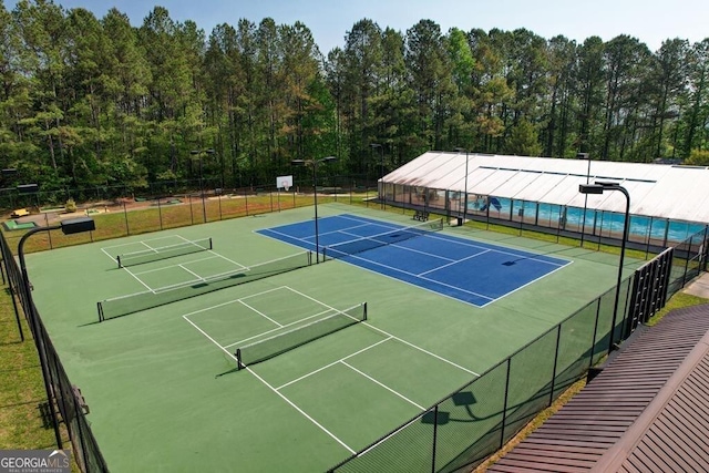 view of tennis court featuring fence and a view of trees