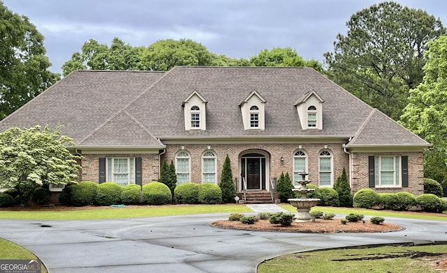 view of front of home featuring driveway, brick siding, and roof with shingles