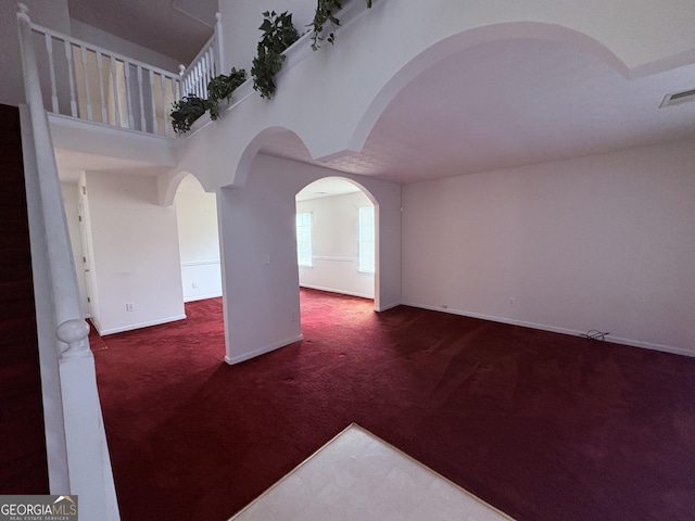 carpeted empty room with baseboards, a towering ceiling, and visible vents