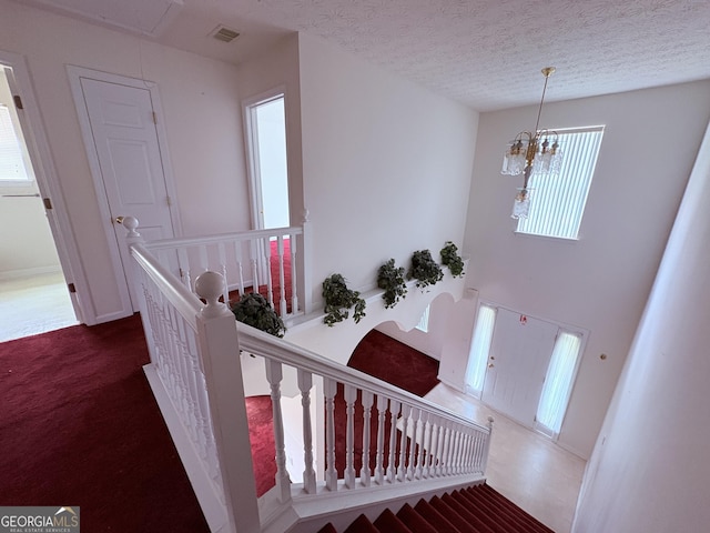 stairs with attic access, a textured ceiling, visible vents, an inviting chandelier, and carpet flooring