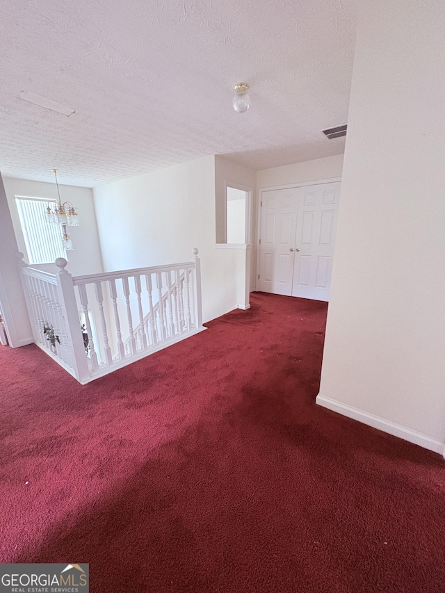 unfurnished room with a textured ceiling, visible vents, baseboards, a notable chandelier, and carpet flooring
