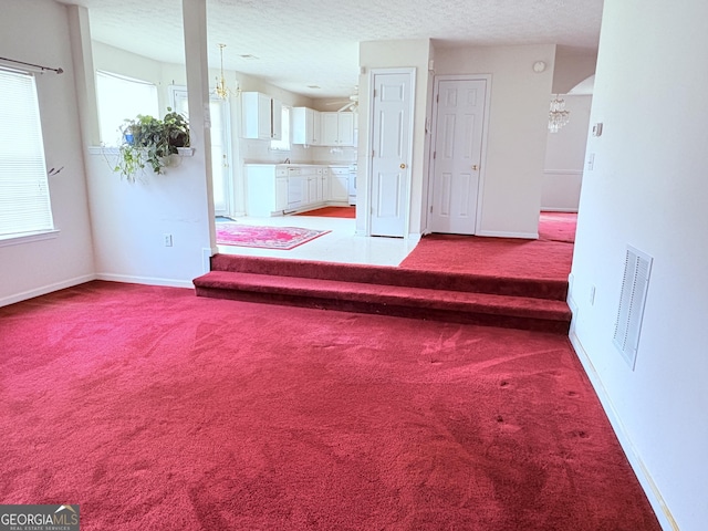 unfurnished room with baseboards, light colored carpet, a textured ceiling, and a notable chandelier