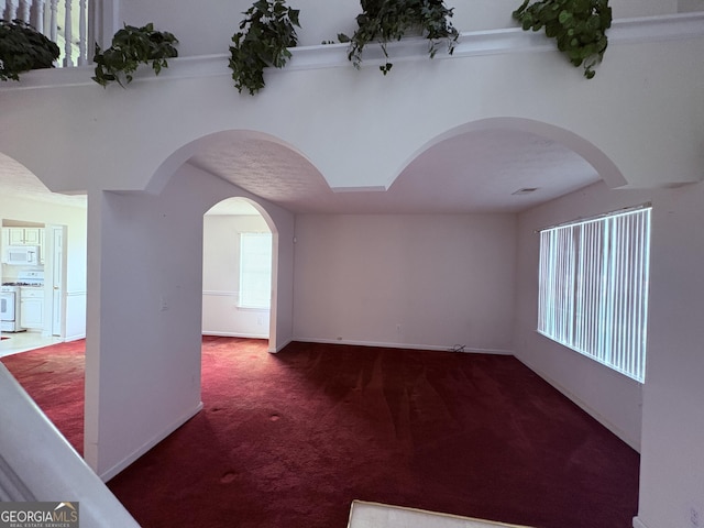 carpeted spare room with baseboards and arched walkways