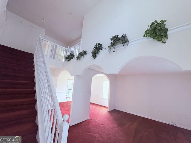 staircase featuring arched walkways, baseboards, carpet, and a high ceiling