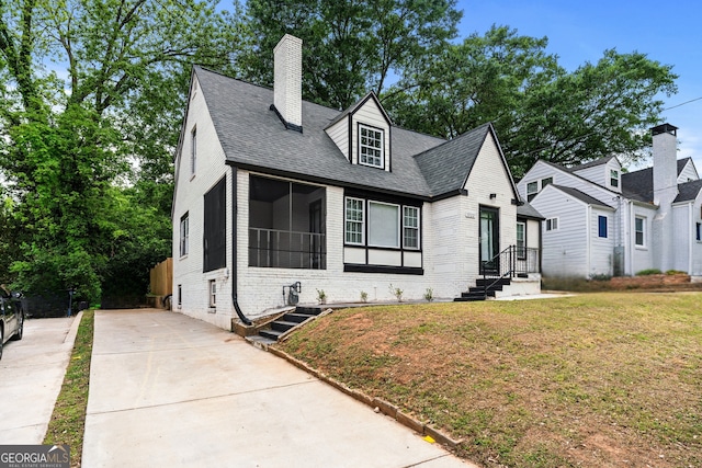 view of front of property with a chimney, brick siding, a front lawn, concrete driveway, and a shingled roof