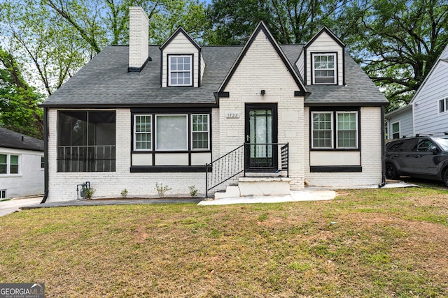 cape cod house with a chimney, a shingled roof, a front yard, and brick siding