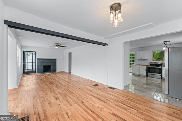 unfurnished living room with visible vents, a tile fireplace, baseboards, ceiling fan with notable chandelier, and light wood finished floors