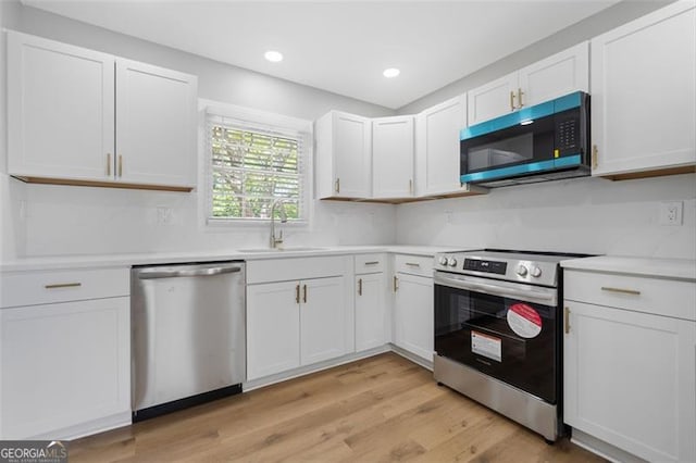 kitchen featuring light wood finished floors, stainless steel appliances, a sink, white cabinetry, and light countertops