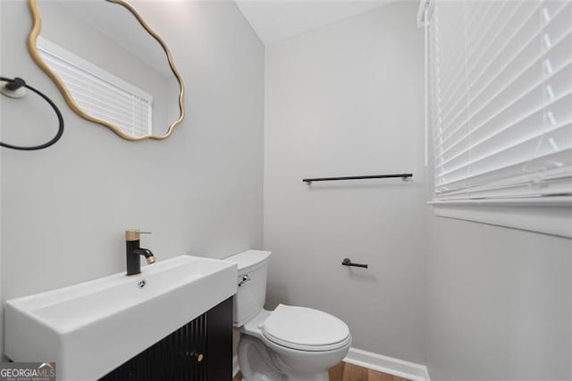 half bathroom featuring baseboards, wood finished floors, vanity, and toilet
