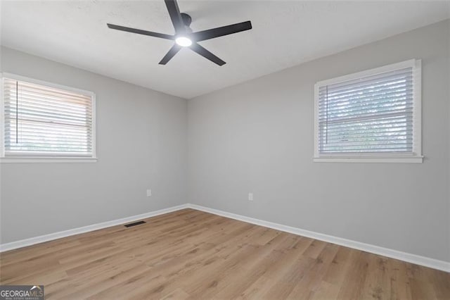 empty room featuring light wood-style floors, plenty of natural light, visible vents, and a ceiling fan