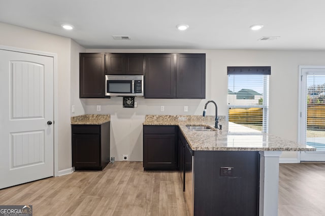 kitchen with a peninsula, a sink, stainless steel microwave, visible vents, and light stone counters