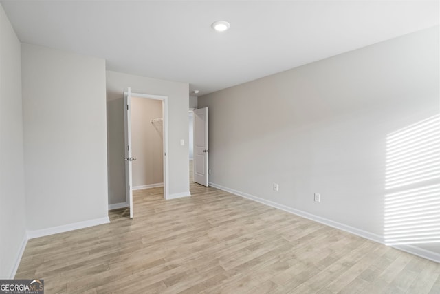 unfurnished bedroom featuring light wood-style flooring, baseboards, and a walk in closet